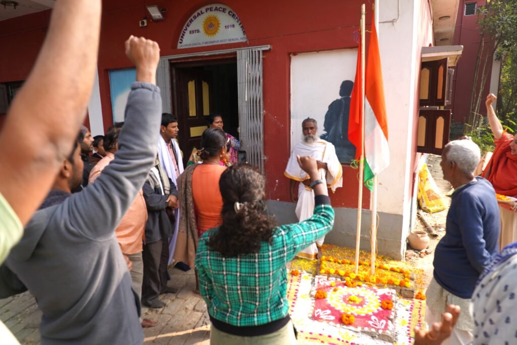Devotees celebrating India's 77th Republic Day at Universal Peace Centre ashram, Lachipur, West Bengal on January 26, 2026 – group hoisting Indian Tricolour flag with raised fists, Swamiji in white robes, garlanded podium with marigolds, Sunyoga emblem, patriotic unity after Sunyoga Healing Course