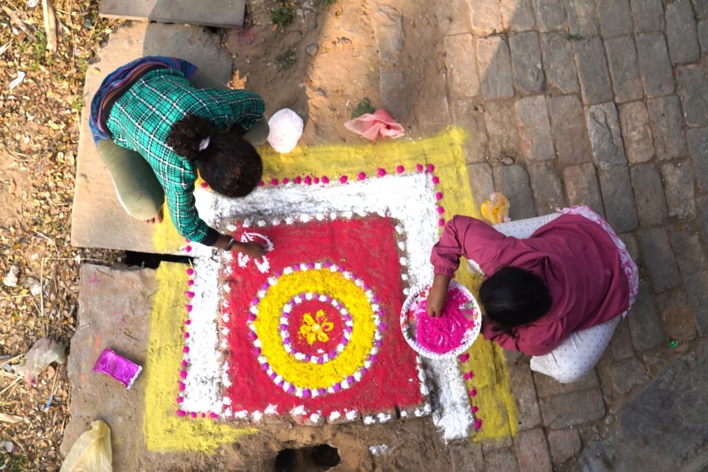 Two young women devotees creating vibrant yellow-white rangoli floral design with marigold petals and colored powders during Republic Day celebrations at Universal Peace Centre ashram, Lachipur, West Bengal 2026 – Sunyoga spiritual event preparation.